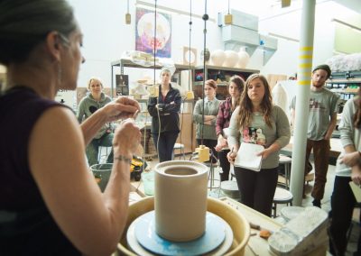 Students watch a wheel throwing demonstration by a visiting artist in a Ceramics class at the Art Lofts.