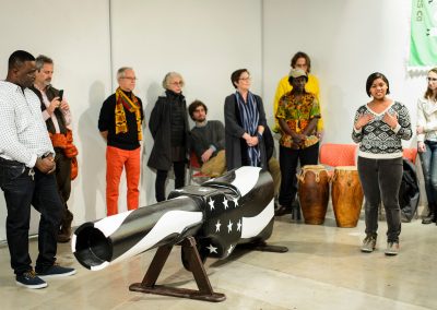 At left, Eric Adjetey Anang (standing at left), Ghanaian woodcarver, master-coffin builder and Windgate Artist in Residence in the Art Department, listens to undergraduate Jamie Dawson, a first-year student in the ninth cohort of the First Wave program, perform a spoken-word piece as part of an opening exhibit of Adjetey Anang's work at the Arts Loft at the University of Wisconsin-Madison. During the event, Adjetey Anang led a gun-breaking ceremony and invited guests to participate in a symbolic breaking of the barrel of his gun-shaped coffin. The gun-breaking action was in support of the Black Lives Matter movement, and against gun violence locally, nationally and internationally.