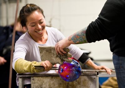 Glass artists Quincy Neri (right) and Yuki Wakamiya (left) work together with an assortment of tools and blown air to shape a piece of molten glass during a demonstration at the Glass Lab open house at University of Wisconsin-Madison.