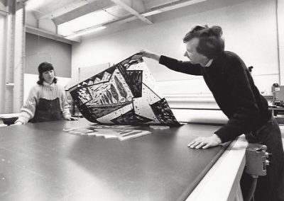 A professor removes a block print from a press with a student watching.