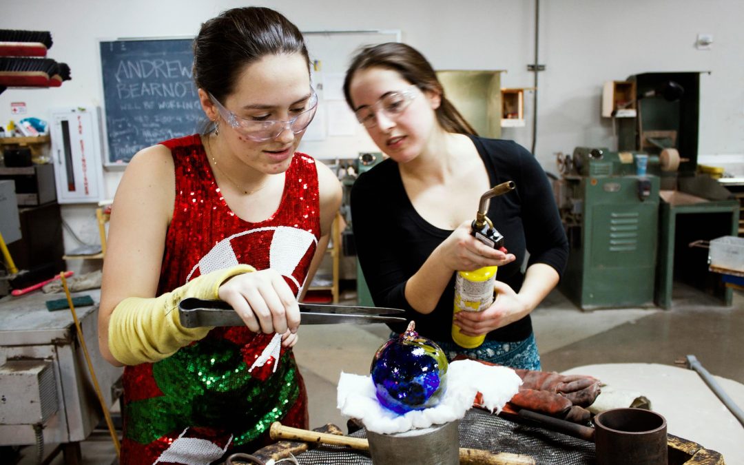 Glass students put the finishing touches on a handmade glass holiday ornament.