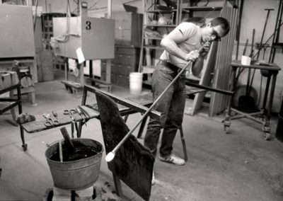 In the hot glass lab, art student Rick Findora blows air into the blowpipe to create a bubble in the molten glass on the end in the November of 1985. Findora graduated with a BFA in 1986.