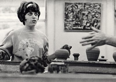 An art student in a Wisconsin Bucky sweatshirt works with clay at a pottery wheel, ca. 1965.