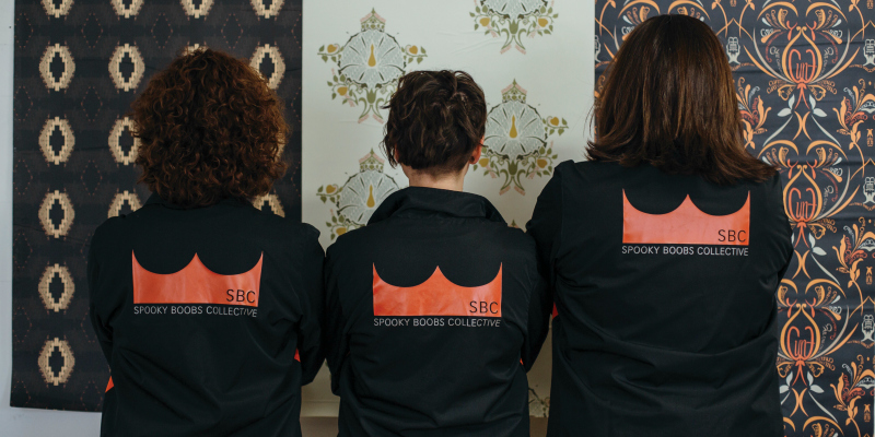 A photo of the backs of the members of the Spooky Boobs Collective, wearing matching black jackets.