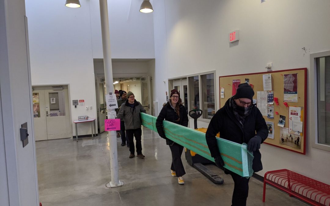 Six people carry a long painting by Professor Buisch out of the Art Lofts building. Photo by Dan Fitch.