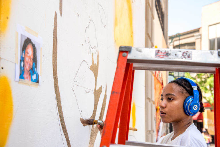 Shiloah Coley, 21, looks at a reference photo of Aiyana Mo'Ney Stanley Jones as she paints a mural outside the Overture Center in downtown Madison, Wis., on June 11, 2020. Stanley was seven years old when she was shot and killed in a police raid in Detroit, Mich., in 2010. Coley used Stanley and the likenesses of other young Black people killed by police as the inspiration for the figures in her murals. Coley, originally from the suburbs of Chicago, is a recent graduate from the University of Wisconsin-Madison, where she studied public art and the criminalization of graffiti and other forms of artistic expression. "I've always believed in the arts as a super transformative thing." "I wanted [this mural] to be two black teenagers with a confrontational gaze. People need to reckon with black people in this space and taking up space in Madison."