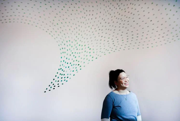 UW-Madison’s Helen Lee, standing in front of her wall-sized artwork “Brood,” composed of “generations” of glass cicadas with deep cultural meaning on exhibit through March 7 at the Arts + Literature Laboratory.