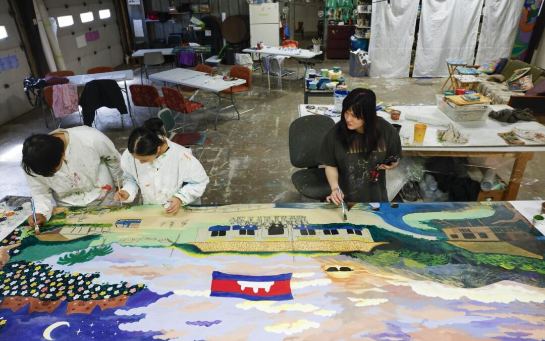 Working at the DAMA Mural Shop on Allis Avenue, Chan Hen, Hanna Tran and Rin Ma help paint a mural designed from drawings made by sixth grade students at a rural Cambodian school. The mural will be shipped back to Cambodia and installed on an outside wall at the school built by Sarith Ou. Photo by Ruthie Hauge.