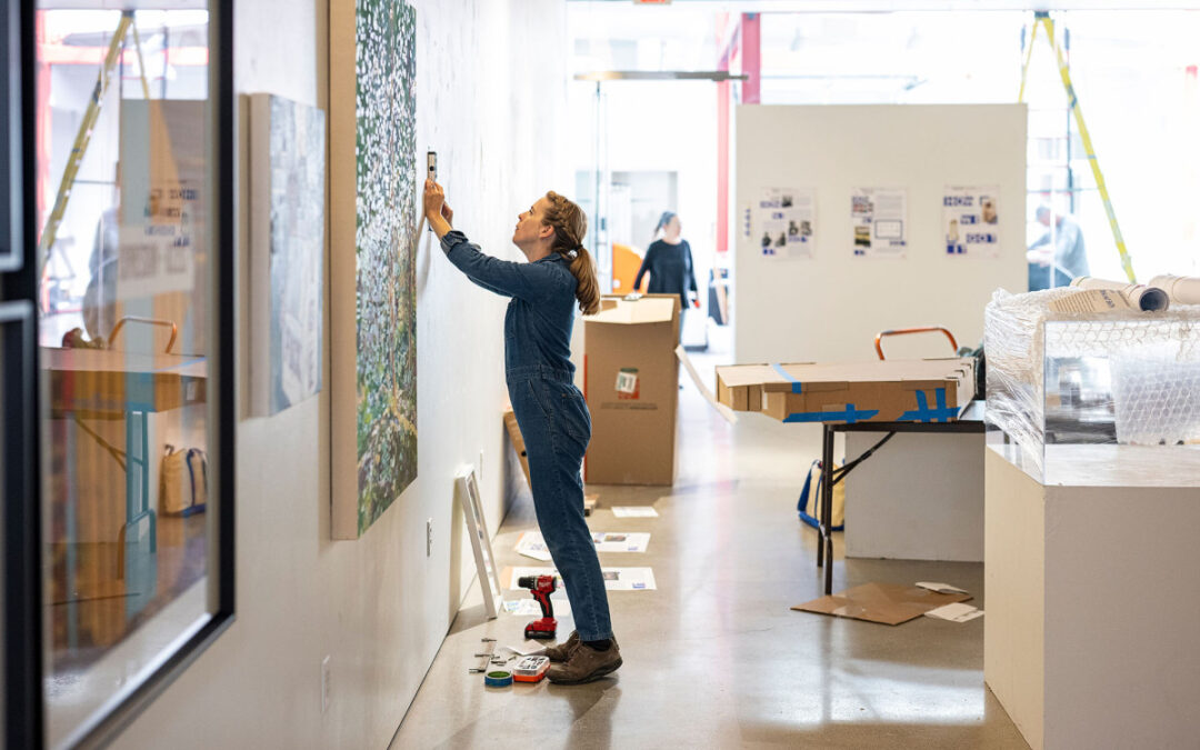 Emily Belknap (installing an artwork above) is one of more than 100 UW–Madison alumni artists featured in “How We Got It Together,” a massive campus exhibition curated by Professor Emerita Laurie Beth Clark.