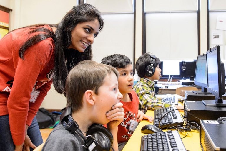 A volunteer instructor works with students on a computer program