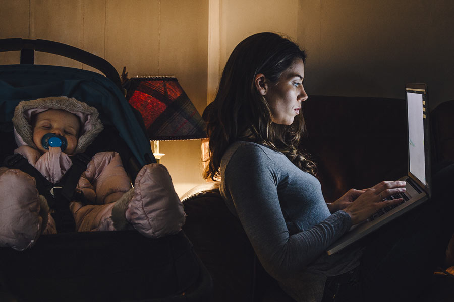 woman working on a laptop in the dark with her baby sleeping next to her