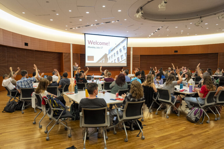people sitting around tables, gathered at a presentation or conference.