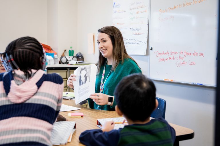 Student teacher holding a paper and talking to two young students.